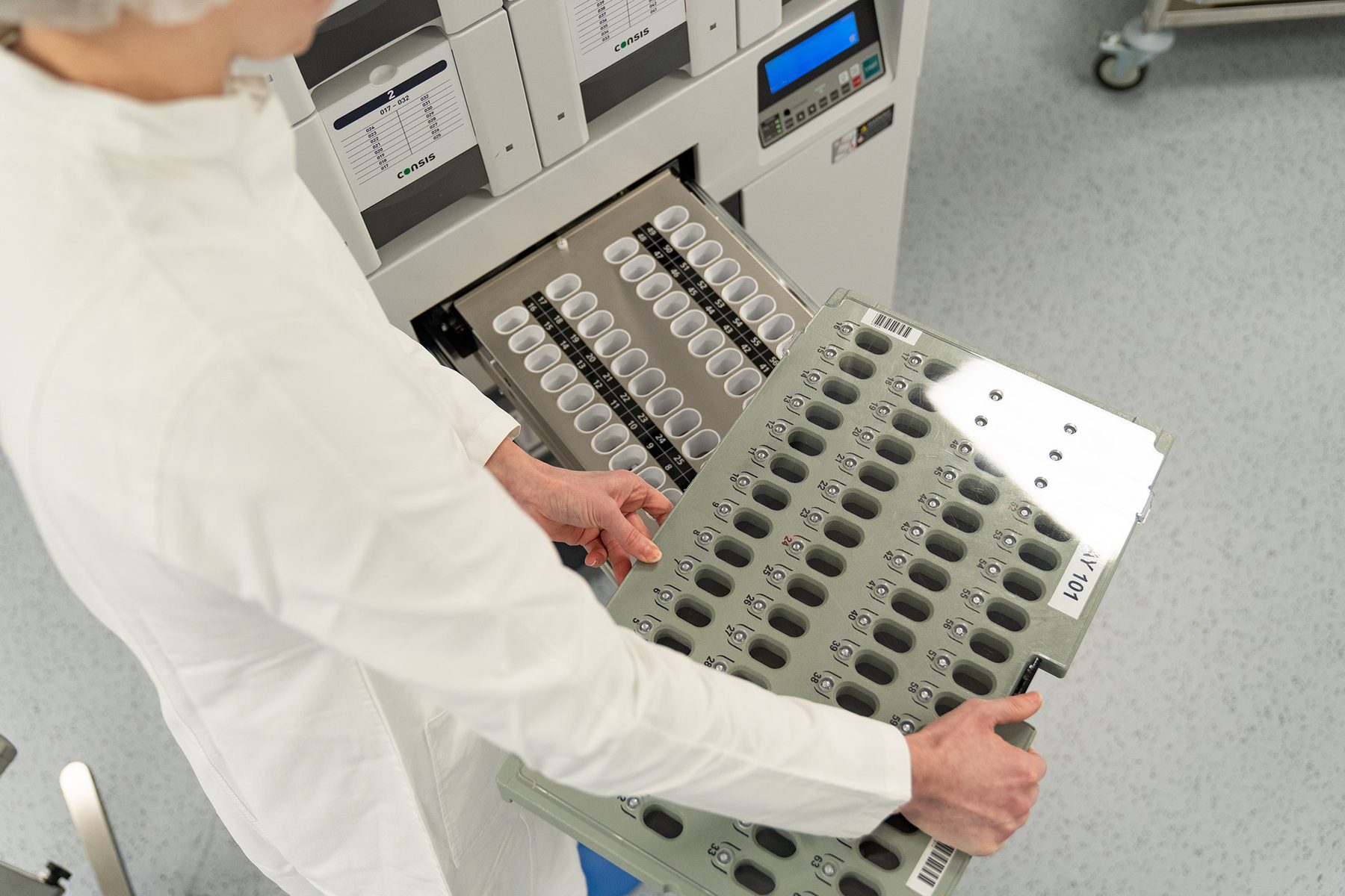 Mitarbeiterin im Kittel zieht einen Kassettenträger aus der geöffneten Schublade der Verblisterungsanlage